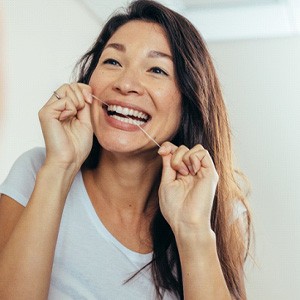 Woman smiling while flossing teeth at home