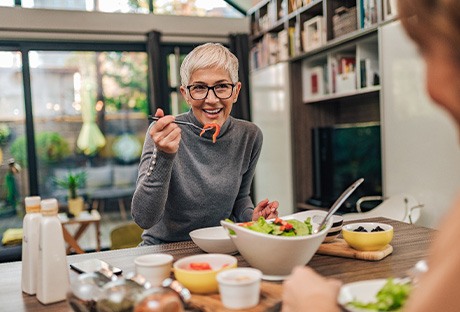 Woman with black glasses smiling while eating with friend