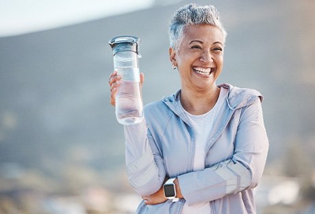 Woman smiling with water bottle on hike outside