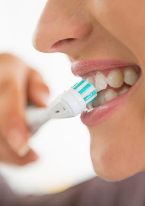 Woman brushing teeth to care for fixed bridge