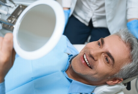 Man with dental implants looking at smile in the mirror