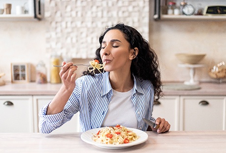 Woman enjoying pasta in kitchen at home