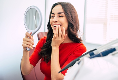 Woman smiling at reflection in handheld mirror