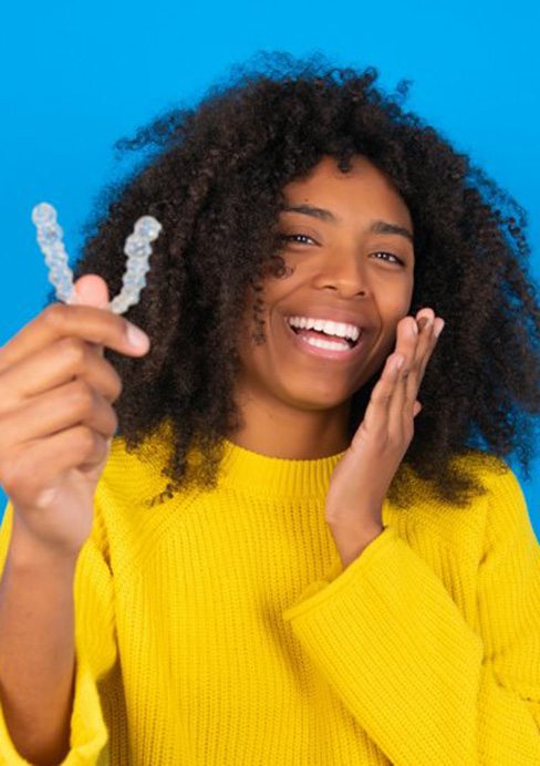 Woman smiling while holding up an Invisalign aligner