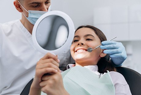 Teen smiling in small mirror with the dentist standing nearby