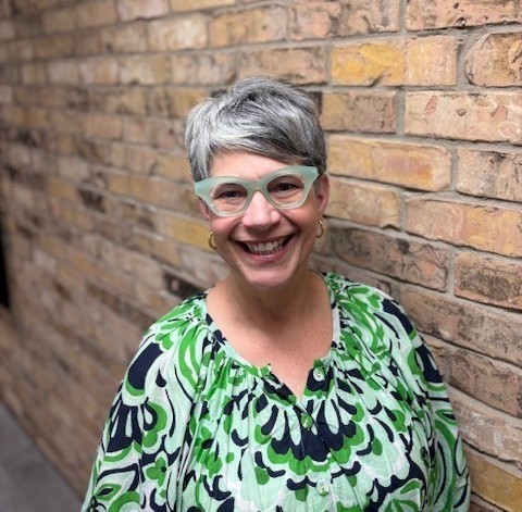 Doctor Kimber Holmes smiling with brick wall as the background.